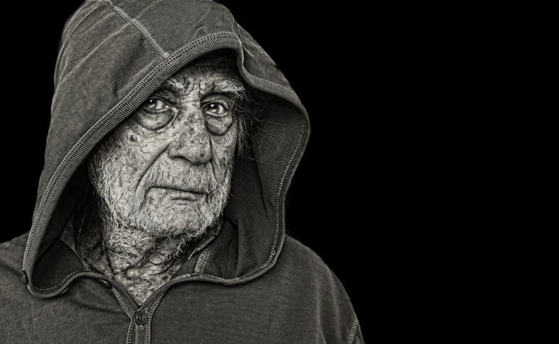 An elderly man with a weathered face, deep wrinkles, and piercing eyes wears a hooded sweatshirt, staring intensely. His expression is solemn and mysterious. Image titled 'Candle Face Victim 30: Candle Face's Congregation.'