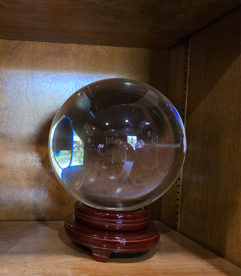 A polished crystal ball resting on a wooden stand, reflecting a dimly lit room. The mystical object hints at the possibility of a connection between Candle Face and Arthur Mills, as explored in Candle Face Chronicles.